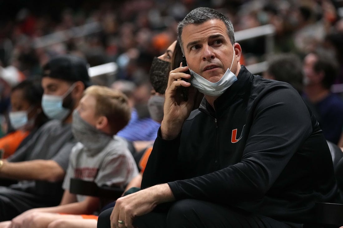 Feb 2, 2022; Coral Gables, Florida, USA; Miami Hurricanes head football coach Mario Cristobal talks on a phone while sitting court-side during the second half between the Miami Hurricanes and the Notre Dame Fighting Irish at Watsco Center. Mandatory Credit: Jasen Vinlove-USA TODAY Sports