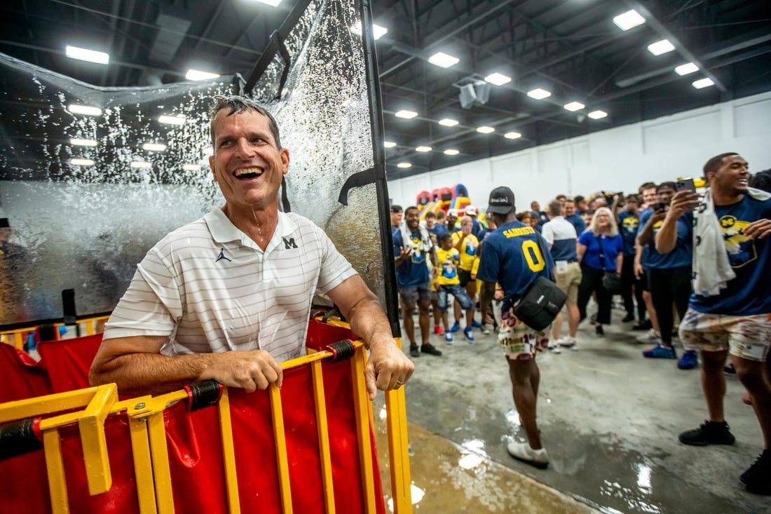 Michigan head coach Jim Harbaugh reacts after being knocked into a dunk tank for the first time during the Maize and Blue Big Top Event Kids Fair at the Dort Event Center in Flint on Thursday, July 21, 2022, as part of the Michigan football state caravan.