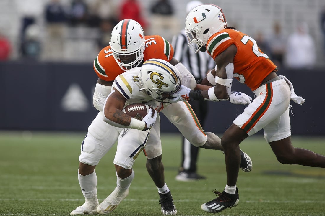Nov 12, 2022; Atlanta, Georgia, USA; Georgia Tech Yellow Jackets running back Dontae Smith (4) has his face masked grabbed by Miami Hurricanes cornerback Te'Cory Couch (23) as linebacker Wesley Bissainthe (31) attempts to make a tackle in the second quarter at Bobby Dodd Stadium. Mandatory Credit: Brett Davis-USA TODAY Sports
