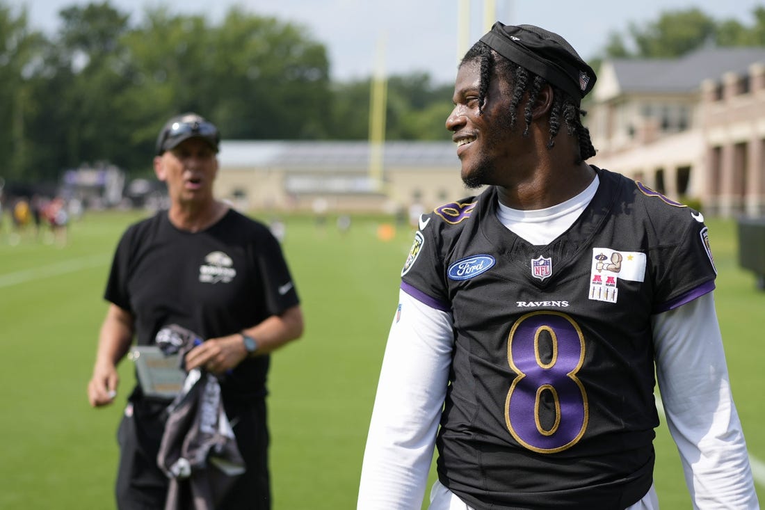 Jul 27, 2023; Owings Mills, MD, USA; Baltimore Ravens quarterback Lamar Jackson (8) smiles at a fan with Baltimore Ravens offensive coordinator Todd Monken standing in the background following training camp practice at Under Armour Performance Center. Mandatory Credit: Brent Skeen-USA TODAY Sports