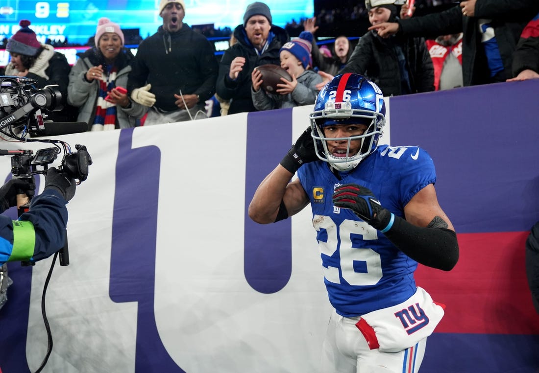 New York Giants running back Saquon Barkley (26) is shown after scoring a touchdown and giving the ball to Harrison Isaacs (background), 6. Harrison traveled with his father Christoper Isaacs (background) to attend his first NFL game, Sunday, January 7, 2024.